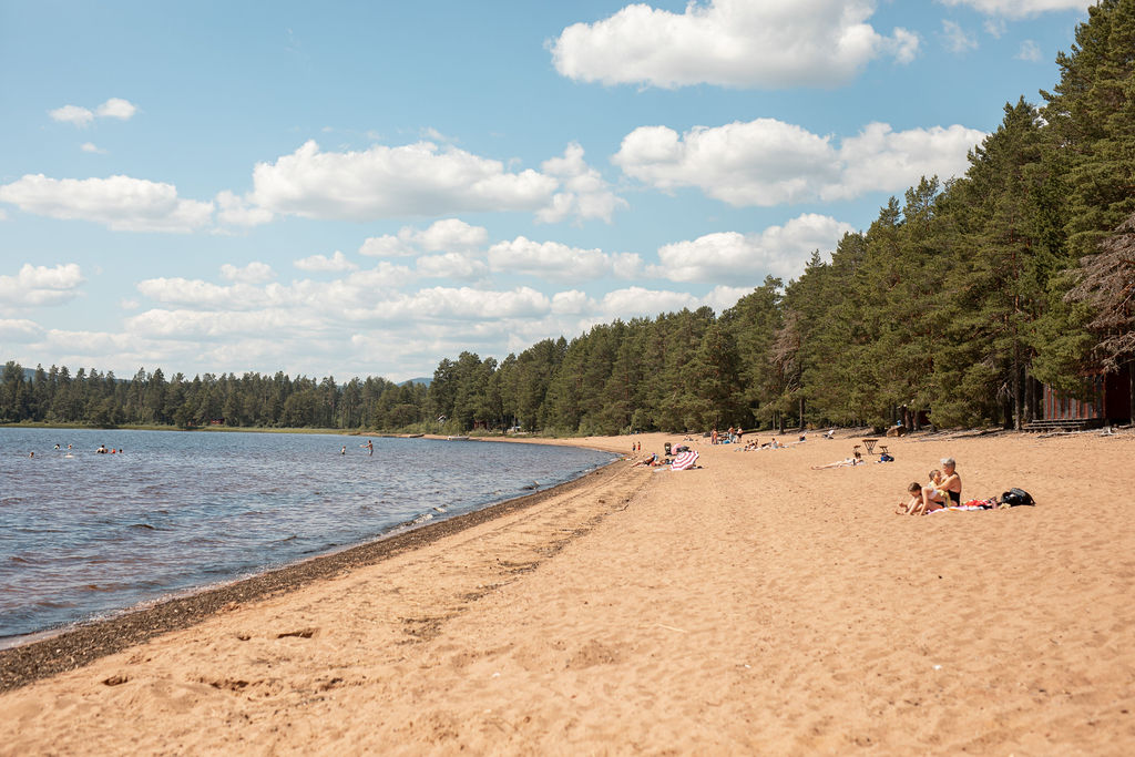 Badande människor vid sjöstrand nära Vansbro